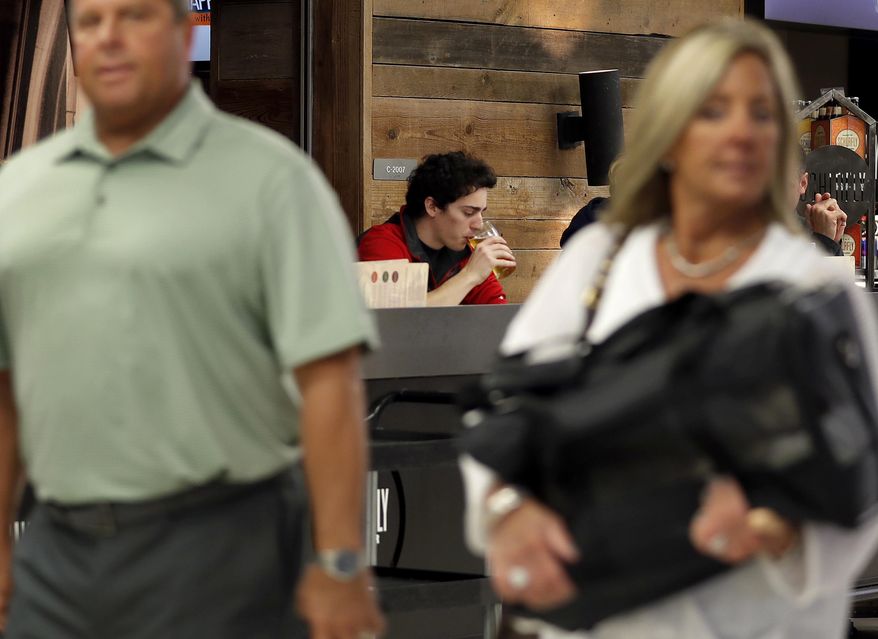 In this photo made Friday, Feb. 24, 2017, traveler Dominic Maley, center, sips on a beer while waiting to board a flight as others pass by at St. Louis Lambert International Airport in St. Louis. The Missouri House has passed a proposal that would allow people to bring alcohol out of airport bars and restaurants to gates. (AP Photo/Jeff Roberson)