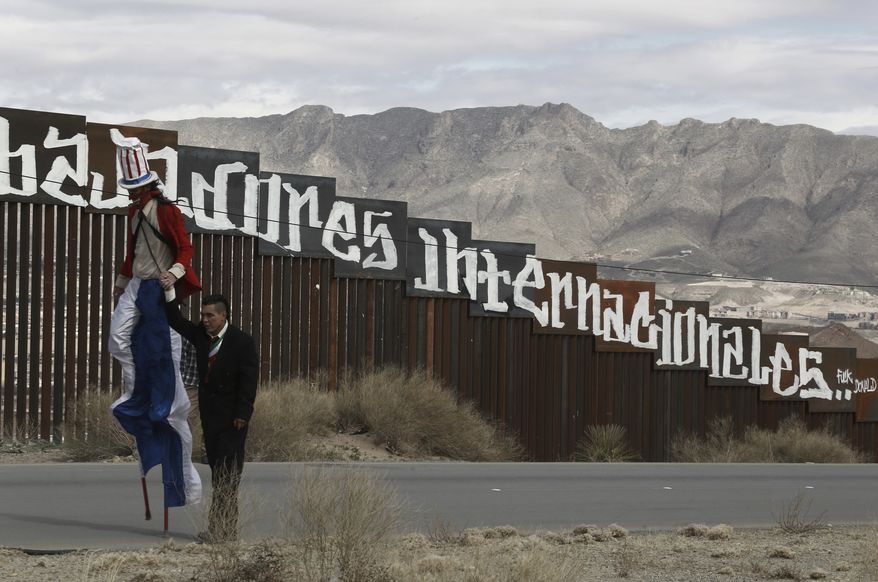 Protestors dressed as a diabolical Uncle Sam, on stilts, and Mexico&#39;s President Enrique Pena Nieto hold hands as they walk along the border fence in Ciudad Juarez, Mexico Sunday, Feb. 26, 2017. A group of about 30 protestors gathered to paint slogans on the border wall and stage a performance mocking the relationship between Pena and President Donald Trump. The partial message in Spanish behind reads: &quot;Neither delinquents nor illegals, we are international workers.&quot; (AP Photo/Christian Torres)
