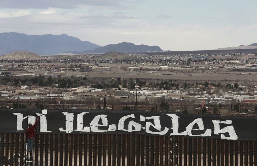 Sunland Park, New Mexico, is seen over the U.S. border fence as a protestor finishes painting the Spanish slogan "Neither delinquents nor illegals, we are international workers" on the Ciudad Juarez, Mexico side of the fence, Sunday, Feb. 26, 2017. A group of around 30 protestors gathered to paint messages on the border wall on the outskirts of Ciudad Juarez and stage a performance mocking the relationship between Presidents Donald Trump and Enrique Pena Nieto. (AP Photo/Christian Torres)