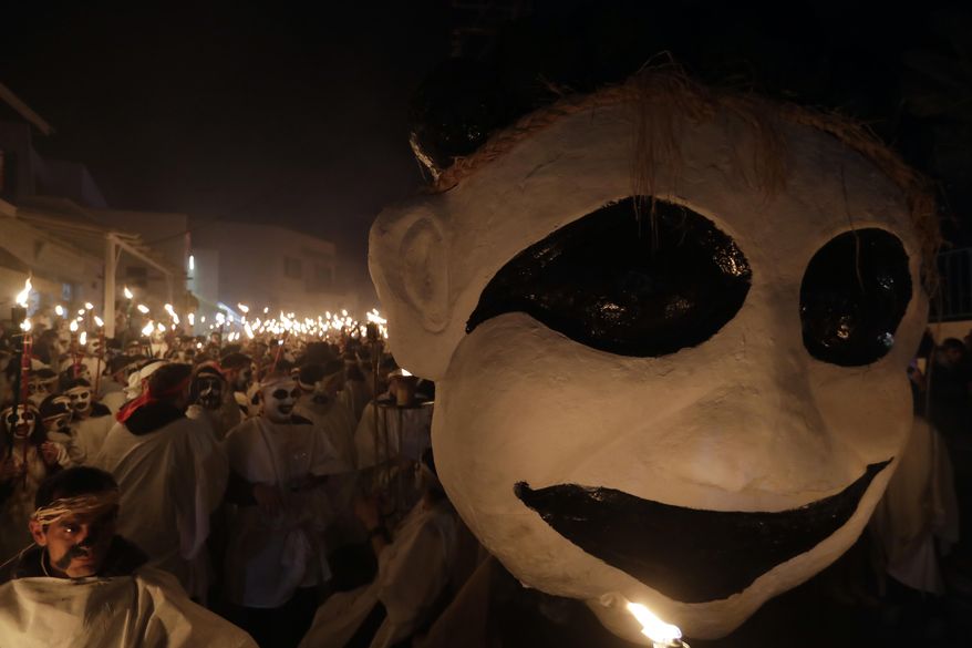 In this photo taken on Saturday, Feb. 25, 2017 young men and women with faces painted to resemble black-and-white masks wear white sheets and hold torches on long poles take part at the Torch Parade on the Greek island of Naxos. About 2,000 people took part at the famous, and very popular, Lampadiforia (Torch Parade). (AP Photo/Thanassis Stavrakis)