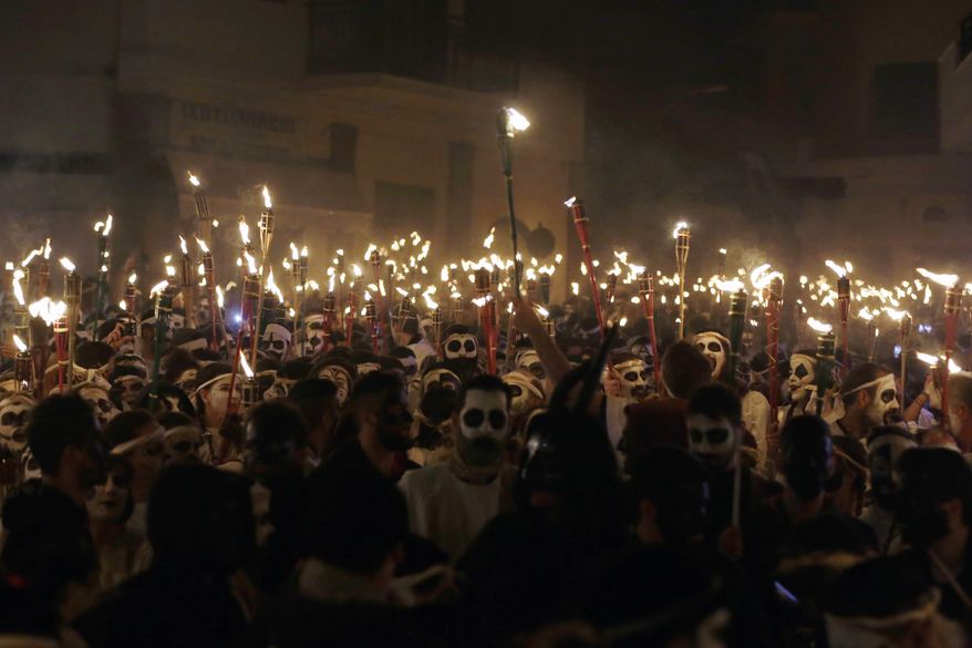 In this photo taken on Saturday, Feb. 25, 2017 young men and women with faces painted to resemble black-and-white masks wear white sheets and hold torches on long poles take part at the Torch Parade on the Greek island of Naxos. About 2,000 people took part at the famous, and very popular, Lampadiforia (Torch Parade). (AP Photo/Thanassis Stavrakis)