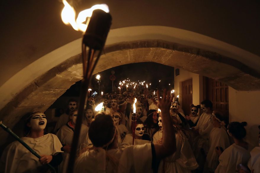 In this photo taken on Saturday, Feb. 25, 2017 young men and women with faces painted to resemble black-and-white masks wear white sheets and hold torches on long poles take part at the Torch Parade on the Greek island of Naxos. About 2,000 people took part at the famous, and very popular, Lampadiforia (Torch Parade). (AP Photo/Thanassis Stavrakis)