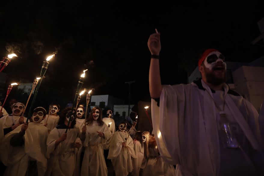 In this photo taken on Saturday, Feb. 25, 2017 children with faces painted to resemble black-and-white masks wear white sheets and hold torches on long poles, as they sing during the Torch Parade on the Greek island of Naxos. (AP Photo/Thanassis Stavrakis)