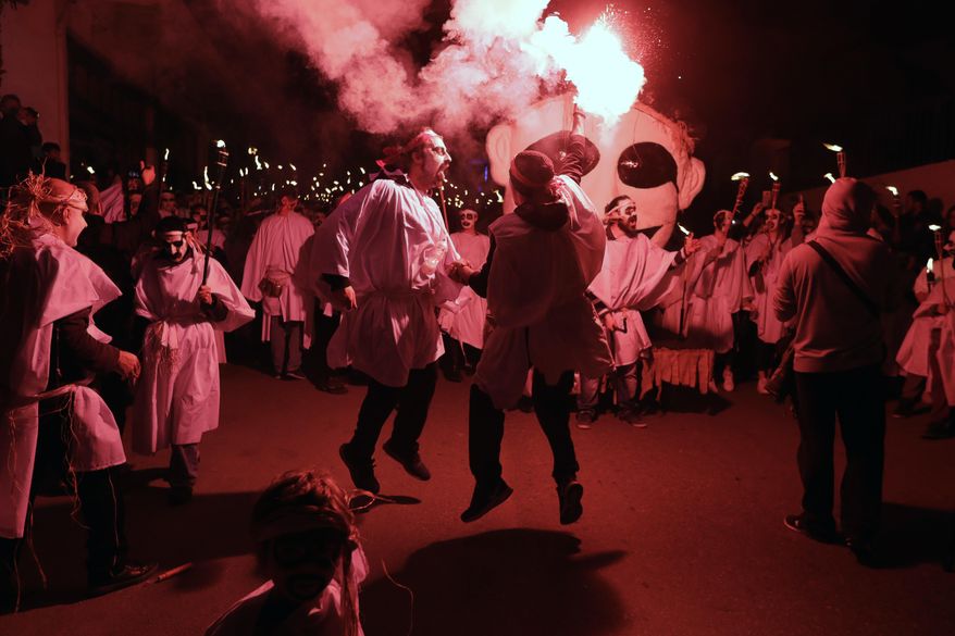 In this photo taken on Saturday, Feb. 25, 2017 two men sing and dance during the Torch Parade on the Greek island of Naxos. Almost 2,000 people took part in the procession of young men and women with faces painted to resemble black-and-white masks wear white sheets and hold torches on long poles. (AP Photo/Thanassis Stavrakis)