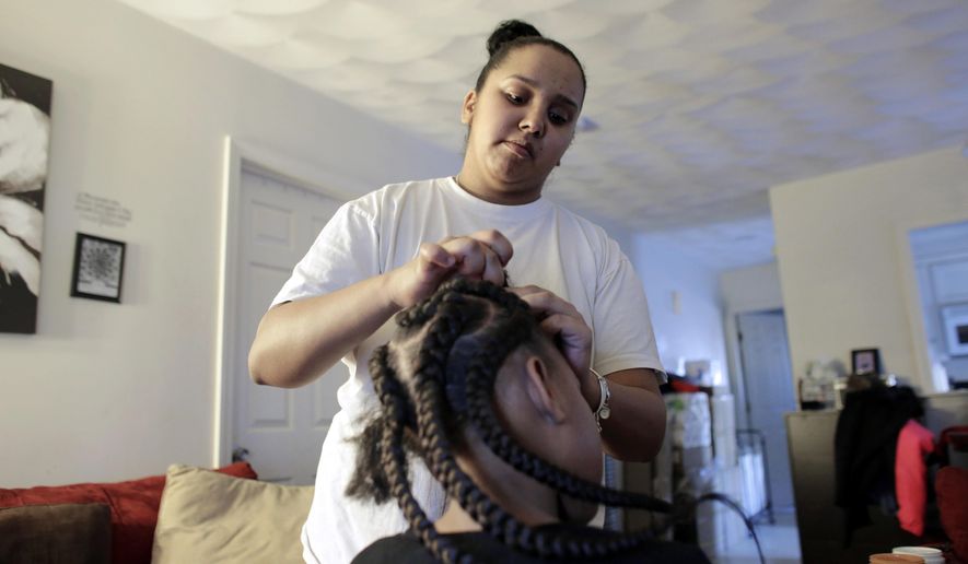 In this Sunday, Feb. 19, 2017 photo Jocelyn DoCouto, top, adds braid extensions for seven-year-old Zanyrah Parrott, of Pawtucket, R.I., in DoCouto's home, in Pawtucket. The billionaire industrialist Charles Koch might not have a lot in common with DoCouto, but they are both part of a national movement to deregulate the business of African-style braiding. DoCouto is pushing for state legislation in Rhode Island that would exempt her from the cumbersome and expensive occupational licensing requirements for hairdressers and barbers. (AP Photo/Steven Senne)