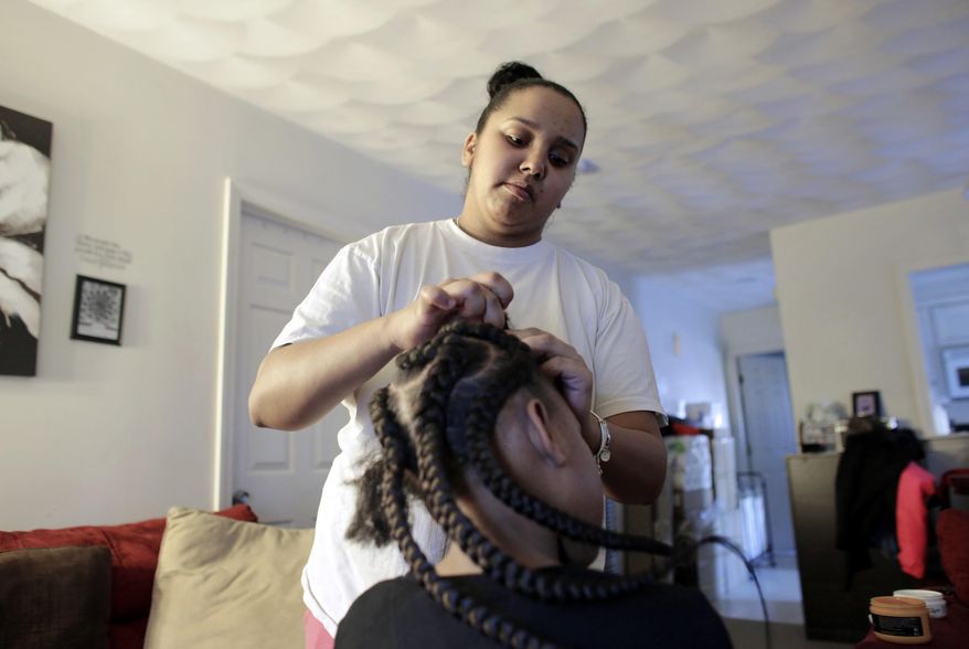 In this Sunday, Feb. 19, 2017 photo Jocelyn DoCouto, top, adds braid extensions for seven-year-old Zanyrah Parrott, of Pawtucket, R.I., in DoCouto's home, in Pawtucket. The billionaire industrialist Charles Koch might not have a lot in common with DoCouto, but they are both part of a national movement to deregulate the business of African-style braiding. DoCouto is pushing for state legislation in Rhode Island that would exempt her from the cumbersome and expensive occupational licensing requirements for hairdressers and barbers. (AP Photo/Steven Senne)