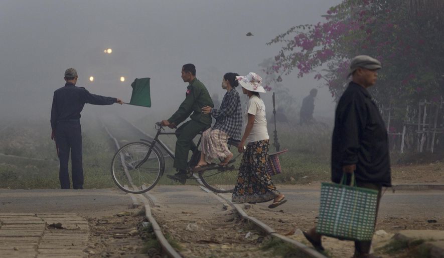 FILE - In this Feb. 8, 2013 file photo, a railway signalman waves a green flag indicating a train to proceed as a man rides a bicycle on the level-crossing close to a suburban train station of Yangon, Myanmar. Developing countries in Asia and the Pacific will need to invest up to $1.7 trillion a year, or $26 trillion through 2030, to meet their infrastructure needs and to maintain the region's growth momentum — more than double the previous estimate in 2009, an Asian Development Bank report said Tuesday, Feb. 28, 2017. (AP Photo/Gemunu Amarasinghe, File)