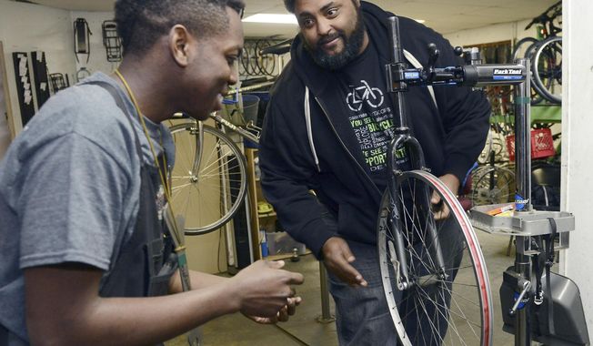 In a Thursday, Feb. 16, 2017 photo, DaiQuan Medley, 19, rushes in to disassemble a bike wheel during a race with other youth mechanics as Sterling Stone, right, lets go of the wheel at Gearin&#x27; Up Bicycles in northeast Washington, D.C. Stone, is the executive director of the non-profit bike shop, founded in 2012, that gives career development opportunities and teaches essential workplace skills to teenagers from underserved communities.  (Rebecca Droke/Pittsburgh Post-Gazette via AP)