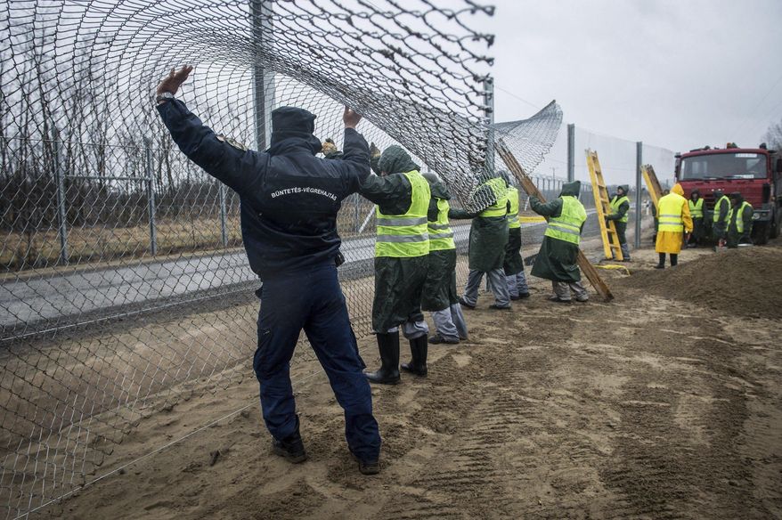 Convicts with the help of a ward, left, build the fence of the second defence line behind the first protective fence on the border between Hungary and Serbia near Kelebia, 178 kms southeast of Budapest, Hungary, Wednesday, March 1, 2017. The Hungarian government decided to construct a second fence along the border with Serbia to prevent migrants' illegal entry into Hungary last Thursday, Febr. 23. (Sandor Ujvari/MTI via AP)