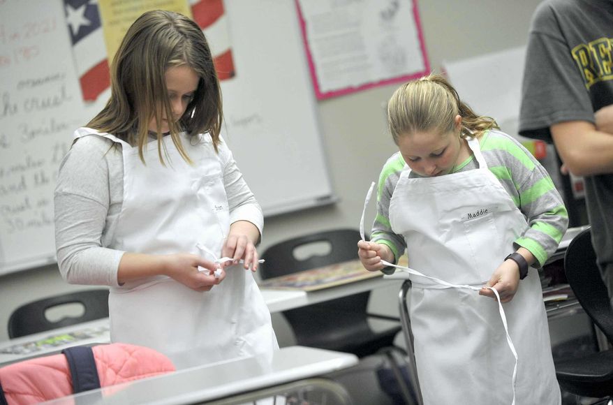 In this Thursday, Jan. 19, 2017 photo, Shylen Hicks, 10, at left, along with Maddie Lee, 10, work on getting their aprons tied and adjusted during the first winter meeting of the Quick Fixin' Young Chefs Club at the Fort Dodge Middle School, in Fort Dodge, Iowa. The club members made a chicken enchilada dip that they gave high ratings to when it was done. (Hans Madsen/The Messenger via AP)