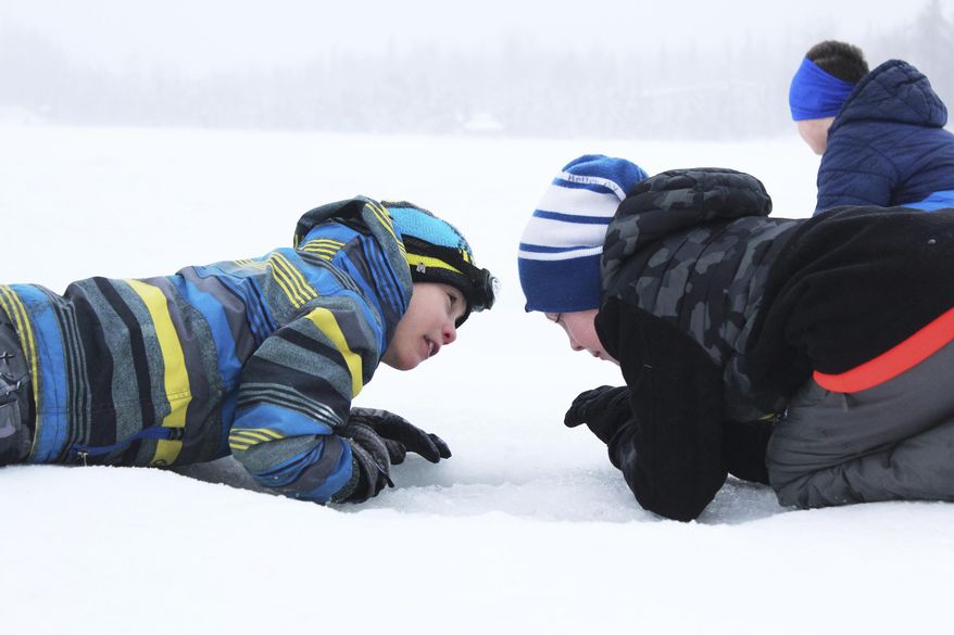 ADVANCE FOR WEEKEND MARCH 4-5, 2017 AND THEREAFTER - In this Feb. 24, 2017 photo, third grader Ryder Lagerson, left, uses his headlight to help his Kaleidescope School of Arts and Sciences classmate Josiah Holloway, right, try to catch a fish during an ice fishing outing at Sport Lake in Soldotna, Alaska. Hundreds of students from multiple Kenai Peninsula School District schools take part in the Alaska Department of Fish and Game's "Salmon in the Classroom" program each year, which includes three ice fishing outings in the winter. (Megan Pacer /Peninsula Clarion via AP)