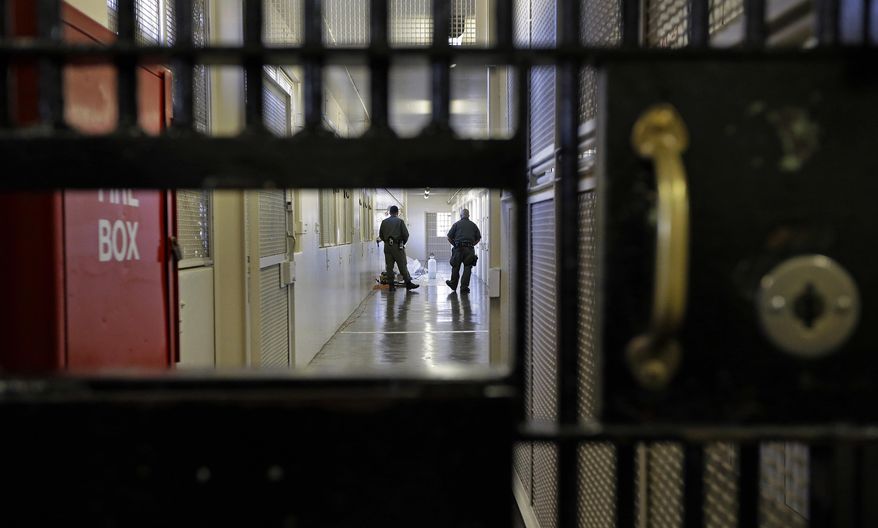 FILE - This Dec. 29, 2015 file photo shows guards walking a corridor in the death row adjustment center at San Quentin State Prison in San Quentin, Calif. A settlement of a lawsuit by inmates against the state of California, obtained by The Associated Press, says the state no longer will keep inmates in the center just for being gang members. Inmates can still be sent to the windowless cells if they are considered an immediate danger. (AP Photo/Ben Margot, File)