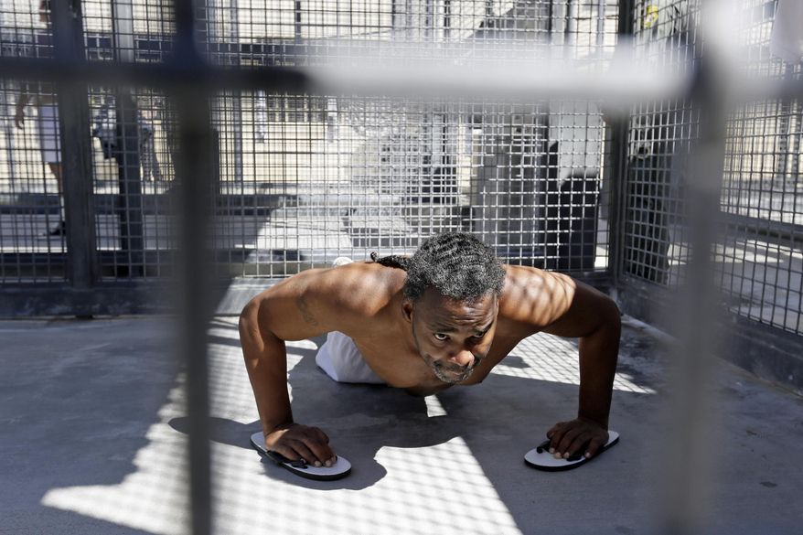FILE - In this Aug. 16, 2016 file photo, condemned inmate Donald DeBose does pushups in a caged recreation yard space of the adjustment center on death row at San Quentin State Prison in San Quentin, Calif. A settlement of a lawsuit by inmates against the state of California, obtained by The Associated Press, says the state no longer will keep inmates in the center just for being gang members. Inmates can still be sent to the windowless cells if they are considered an immediate danger. (AP Photo/Eric Risberg, File)