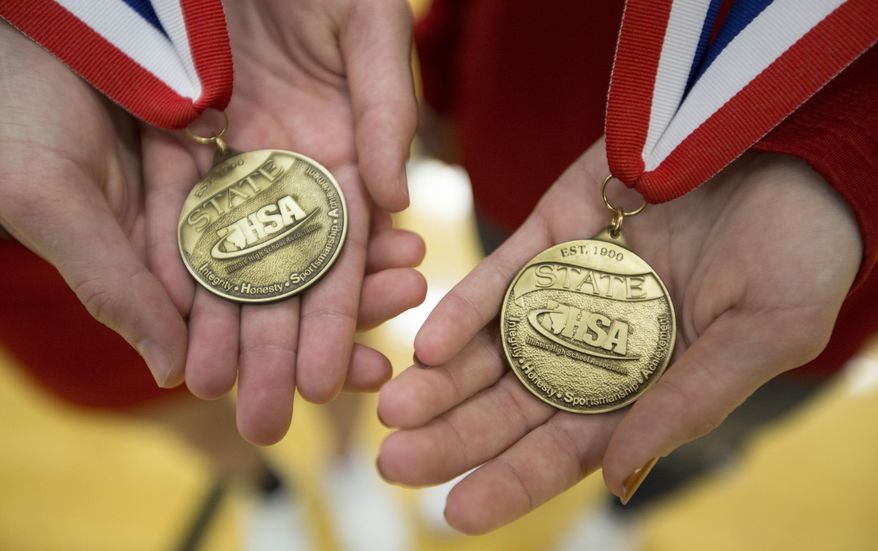 In this Feb. 6, 2017 photo, twins Jordyn Lutzow, and Jenna Lutzow show off their state championship medals at Belvidere North High School in Belvidere, Ill. Jordyn was a champion in competitive cheer and Jenna in cross country this school year. (Arturo Fernandez/Rockford Register Star via AP)