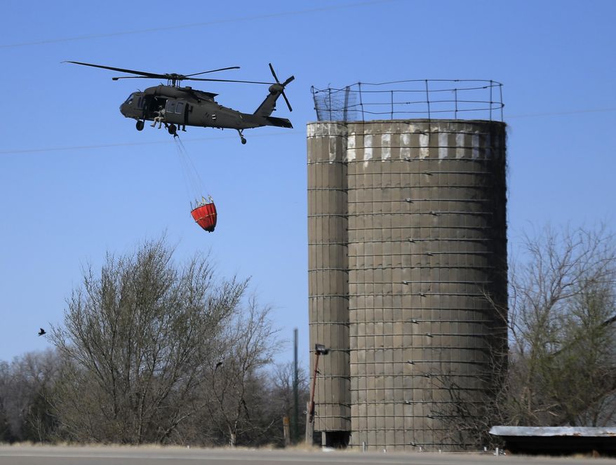 A National Guard helicopter flies past a silo while picking up water from a farm pond near Hutchinson, Kan., Tuesday, March 7, 2017. Emergency crews on Tuesday struggled to contain deadly wildfires that have scorched hundreds of square miles of land in four states and forced thousands of people to flee their homes ahead of the wind-whipped flames. The fires were burning in parts of Kansas, Oklahoma, Texas and Colorado, and warnings that fire conditions were ripe were issued for Iowa, Missouri and Nebraska. (AP Photo/Orlin Wagner)