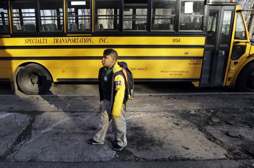 In this Feb. 23, 2017 photo, Justin Beckles stands near a bus at the Martin Luther King Jr. Elementary School in Hartford, Conn. Traditional public schools still educate about half the city’s children, but they are not moving in the same direction as magnet schools with racial integration and academic achievement. (AP Photo/Elise Amendola)
