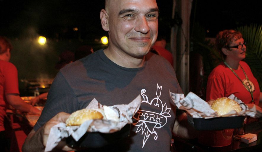 FILE - In this Feb. 24, 2012 file photo, Michael Symon holds his Porky Burgers during the Burger Bash at the Food Network South Beach Wine & Food Festival in Miami Beach, Fla. Celebrity Chef and cookbook author Symon plans to open a restaurant at Cleveland Hopkins International Airport this spring. The Bar Symon restaurant planned for the airport is expected to open in April 2017. (AP photo/Jeffrey M. Boan, File)
