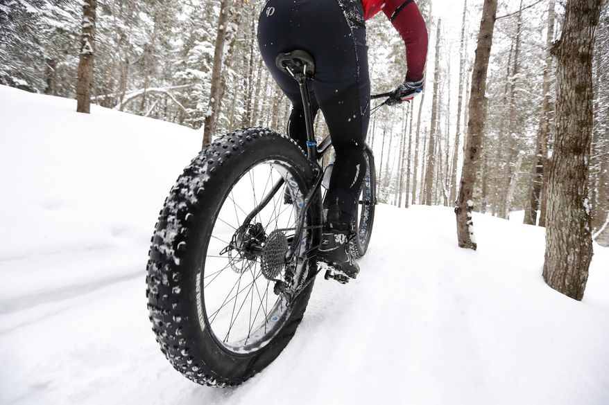 In this Saturday, Feb. 11, 2017 photo a fat tire bicyclist rides on a cross country ski trail during a race at the Sugarloaf ski resort in Carrabassett Valley, Maine. Gone are the days when cyclists had to hang up their bikes the winter. These days, many of them are grinding through winter's snow and spring's mud thanks to trendy new "fat bikes" with extra wide tires. (AP Photo/Robert F. Bukaty)