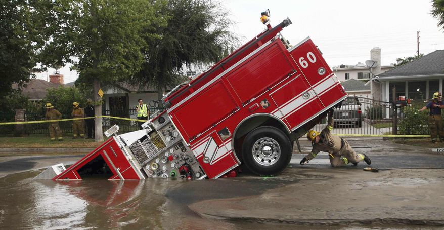 FILE - In this Tuesday, Sept. 8, 2009 file photo, a Los Angeles firefighter looks under a fire truck stuck in a sinkhole in the Valley Village neighborhood of Los Angeles. Four firefighters escaped injury early Tuesday after their vehicle sunk into the hole caused by a burst water main in the San Fernando Valley, authorities said. (AP Photo/Nick Ut)