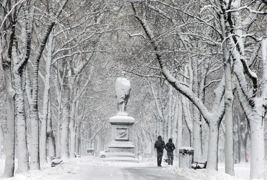 People walk beneath snow-covered trees on the Commonwealth Avenue Mall during a winter storm Tuesday, March 14, 2017, in the Back Bay neighborhood of Boston. (AP Photo/Michael Dwyer)