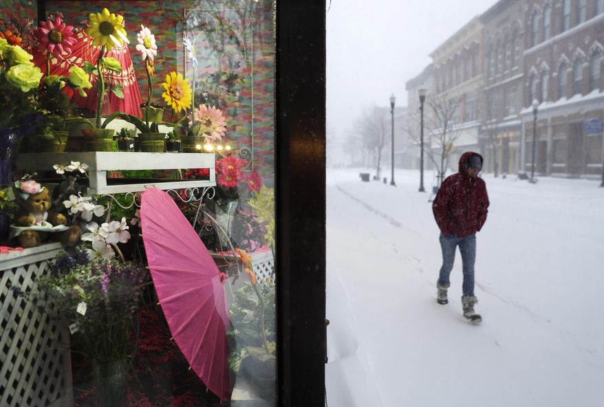 A spring flower display decorates a floral shop window as a pedestrian passes during a snowstorm in Lewiston, Maine, Tuesday, March 14, 2017. A blustery late-season storm is hitting the Northeast, closing schools and prompting dire warnings to stay off the roads. (AP Photo/David Goldman)