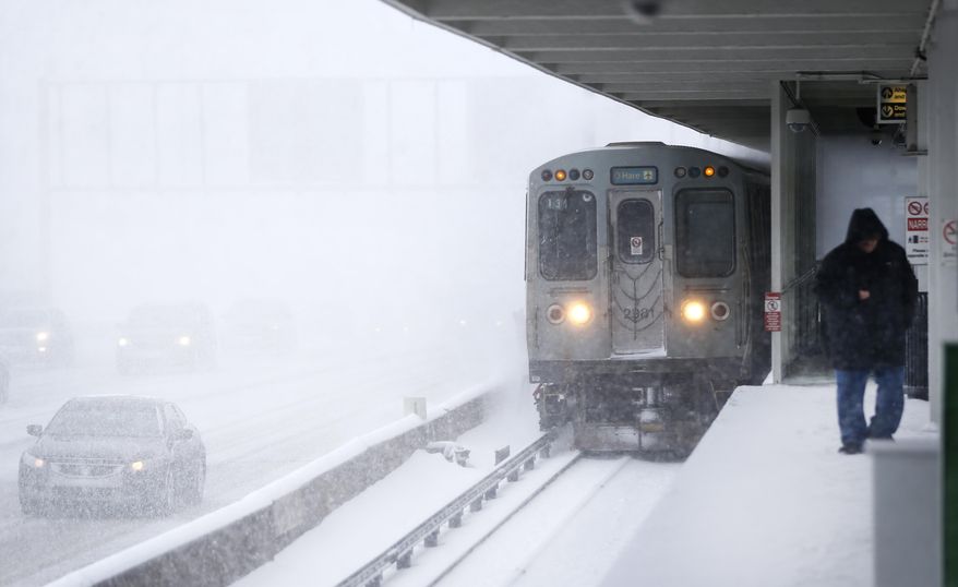 A commuter using the Chicago Transit Authority's Blue Line, braces from the wind and snow as a train heading for O'Hare International Airport approaches the Montrose Station, which runs parallel to the Kennedy Expressway, Tuesday, March 14, 2017, in Chicago. Much of the Midwest and beyond is getting snow as part of a two-day storm that forecasters say will yield between 3 to 6 inches of snow. (AP Photo/Charles Rex Arbogast)