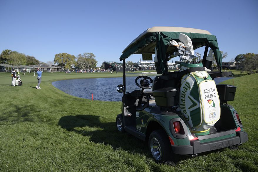 The golf cart and bag belonging to the late golfing great Arnold Palmer sits on a grassy spot next to the 16th tee as Patrick Rodgers hits from the rough alongside the 18th fairway during the first round of the Arnold Palmer Invitational golf tournament in Orlando, Fla., Thursday, March 16, 2017. (AP Photo/Phelan M. Ebenhack)