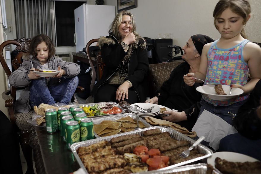 Nadia Hanan Madalo, center, talks with her mother, Alyshooa Kannah, second from right, and other family members as she sits down for a meal in her brother's apartment Thursday, March 16, 2017, in El Cajon, Calif, after arriving to the United States. Madalo and her family, refugees forced to flee their town of Batnaya, Iraq, after the Islamic State invaded and destroyed it several years ago, arrived in San Diego to be reunited with Madalo's siblings and mother. As they flew to the U.S. on Wednesday, a federal judge in Hawaii put a hold on President Trump's newest ban - the latest development in a fight between the administration and the courts that has injected more uncertainty into the lives of refugees. (AP Photo/Gregory Bull)