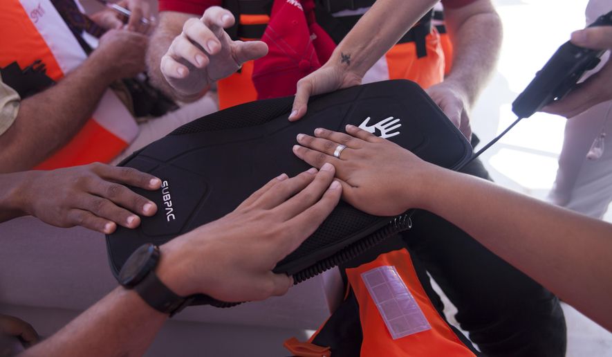 In this Tuesday, March 14, 2017 photo, hearing impaired students place their hands on a Subpac to feel the vibrations from previously recorded whale sounds during a whale watching tour in Samana, Dominican Republic. High-tech backpacks turned whale songs into vibrations, opening the world of whales to hearing impaired children who felt the sounds for the first time. (AP Photo/Tatiana Fernandez)