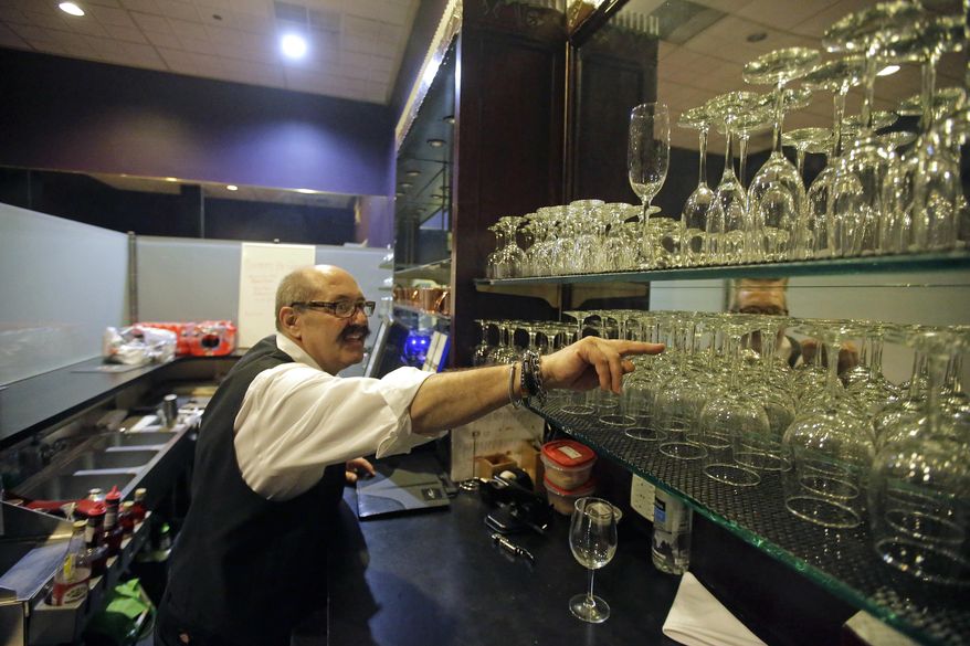 FILE - This Feb. 10, 2017, file photo, a server from Lamb's Grill reaches for a glass behind the "Zion Curtain", in Salt Lake City. Utah restaurants will have more freedom to mix and pour alcohol in front of customers under a measure awaiting Gov. Gary Herbert's signature. But other concessions in the proposal aimed at keeping kids away from bars could complicate restaurant seating and leave some establishments keeping up their frosted glass walls known as "Zion Curtains," used to hide the preparation of drinks. (AP Photo/Rick Bowmer, File)