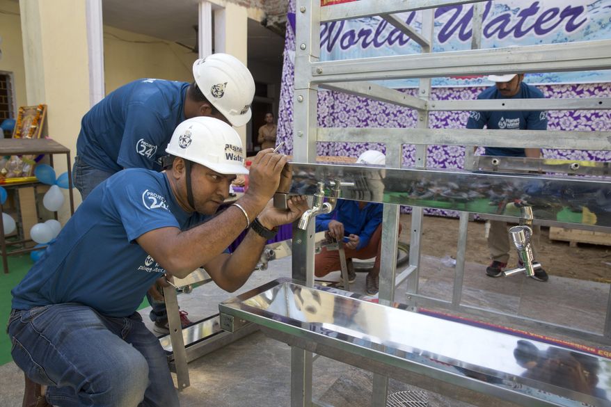 Volunteers of Planet Water foundation, a non-governmental organization based in the U.S. fix taps of a water filtration tower at a school in Nai Basti Village, some 55 kilometers (35 miles) from in New Delhi, India, Wednesday, March 22, 2017. Schoolchildren cheered and village women clapped as a gush of clean water flowed through a set of gleaming steel taps connected to a newly installed water filtration plant in a dusty north Indian village on Wednesday. (AP Photo/Manish Swarup)