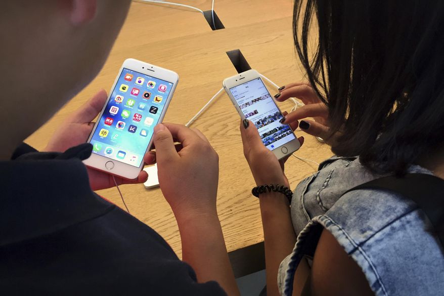 In this Saturday, June 18, 2016, file photo, customers try out Apple iPhone 6s models on display at an Apple Store in Beijing. (AP Photo/Mark Schiefelbein, File)