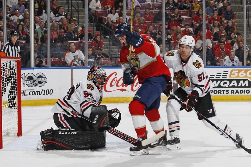 Chicago Blackhawks goaltender Corey Crawford (50) stops a shot by Florida Panthers center Derek MacKenzie (17) as he is checked from behind by Chicago Blackhawks defenseman Brian Campbell (51) during the first period of an NHL hockey game, Saturday, March 25, 2017, in Sunrise, Fla. (AP Photo/Joel Auerbach)