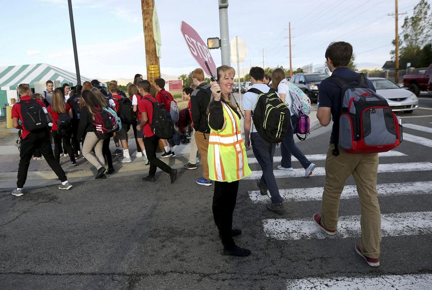 In this Wednesday, Sept. 14, 2016 photo, crossing guard Heather Childs helps students cross the street near Hawthorn Academy and Westvale Elementary School in West Jordan, Utah. School officials in Park City are taking steps to become the first public school district in the state to implement a later start time for high school students who some experts say benefit from more time to sleep in the mornings, the Deseret News reported. (Kristin Murphy/The Deseret News via AP)