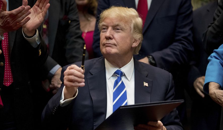President Donald Trump holds up a pen he used to sign one of various bills in the Roosevelt Room of the White House, Monday, March 27, 2017, in Washington. (AP Photo/Andrew Harnik)