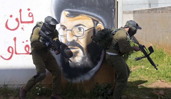 In this Wednesday, March 29, 2017 photo, Israeli soldiers train with paintball guns during a drill at an Army base near Elyakim, Israel. Between myriad concrete buildings with Arabic graffiti that are designed to simulate a typical Lebanese village, dozens of Israeli officers are gearing up for their next battle with Hezbollah guerrillas in the wake of rising tensions between the old adversaries. Arabic is random letters, graffiti depicts Hezbollah's chief Hassan Nasrallah. (AP Photo/Sebastian Scheiner)