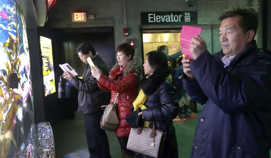 In this March 27, 2017 photo, tourists from China take pictures at the New England Aquarium in Boston. In cities across the country, the American hospitality industry is stepping up efforts to make Chinese visitors feel more welcome. (AP Photo/Elise Amendola)