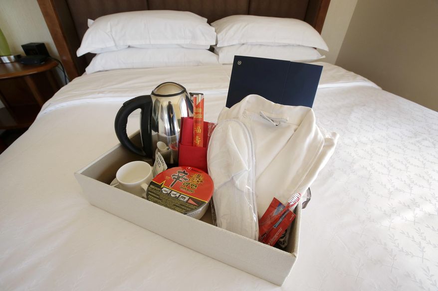 In this March 23, 2017 photo, items in a welcoming kit containing creature comforts that many Chinese travelers expect in their rooms, including, from the left, an electric kettle, green tea, instant noodles, slippers, and a robe, rest in a tray on a bed in a guest room at the Sheraton Boston Hotel in Boston. In cities across the country, the American hospitality industry is stepping up efforts to make Chinese visitors feel more welcome. (AP Photo/Steven Senne)
