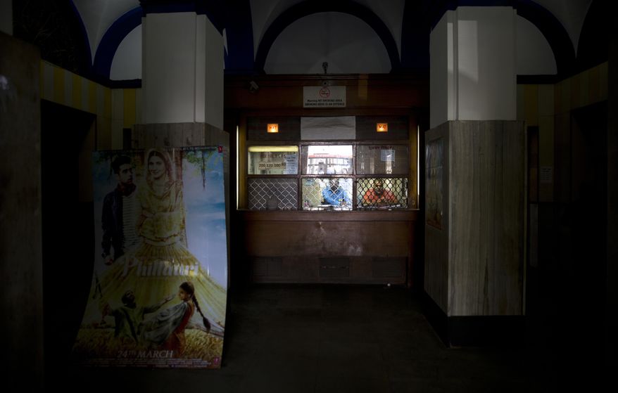 In this Tuesday, March 28, 2017 photo, employees sit at a ticket counter of Regal Theater in New Delhi, India. The Indian capital's iconic theater signed off on Thursday night after more than eight decades with nearly 600 movie buffs cheering a 1964 Bollywood classic at a final screening. It's expected to make way for a multiplex from a single screen. (AP Photo/Manish Swarup)