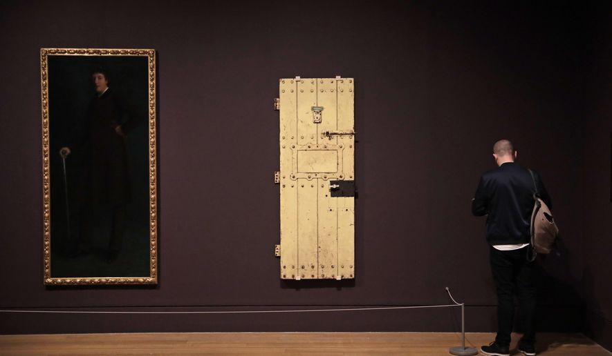 A man stands next to American artist Robert Harper Pennington's "Oscar Wild" painting and the door of Oscar Wilde's prison cell at Reading Jail, during a media preview for the "Queer British Art 1861-1967" exhibition at Tate Britain in London, Monday, April 3, 2017. The show, which opens to the public on Wednesday, includes works that relate to lesbian, gay, bisexual, and trans identities and marks the 50th anniversary of the partial decriminalisation of male homosexuality in England and Wales. (AP Photo/Matt Dunham)