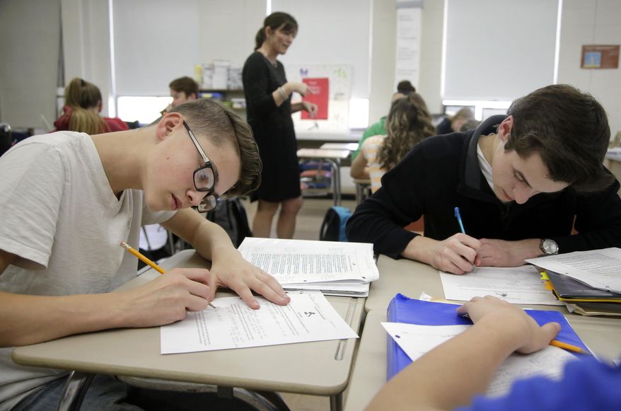 In this Wednesday, March 8, 2017 photo, high school students Jackson Laferriere, left, and Noah Lemoine fill out work sheets as teacher Natalie O'Brien, top center, speaks with students during a civics class called "We the People," at North Smithfield High School in North Smithfield, R.I. More states are requiring graduating high school students to know at least as much about the U.S. founding documents as immigrants passing a citizenship test. (AP Photo/Steven Senne)