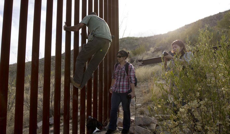 Tim Foley shows how to climb a section of the border wall separating Mexico and the United States near where it ends as journalists Chitose Nakagawa (right) and Marcie Mieko Kagawa look on in Sasabe, Ariz., in this May 11, 2016, photo. Mr. Foley, a former construction foreman, founded Arizona Border Recon, a group of armed volunteers who dedicate themselves to border surveillance. (Associated Press) **FILE**