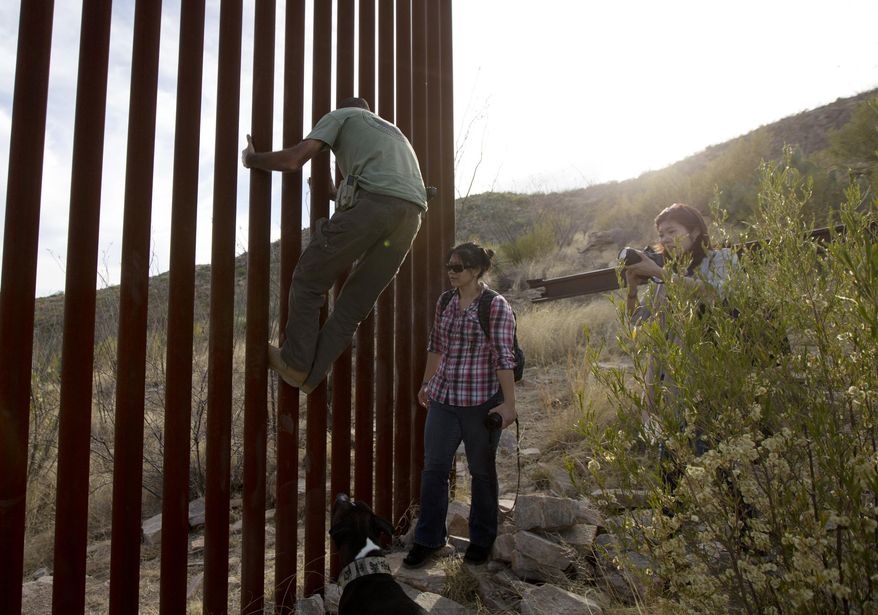 Tim Foley shows how to climb a section of the border wall separating Mexico and the United States near where it ends as journalists Chitose Nakagawa (right) and Marcie Mieko Kagawa look on in Sasabe, Ariz., in this May 11, 2016, photo. Mr. Foley, a former construction foreman, founded Arizona Border Recon, a group of armed volunteers who dedicate themselves to border surveillance. (Associated Press) **FILE**
