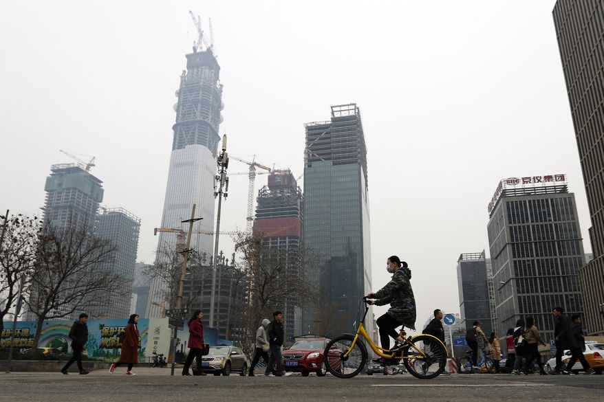 In this Friday, March 17, 2017 photo, a woman rides a bicycle from bike-sharing company Ofo past office buildings during the morning rush hour in the Central Business District of Beijing, China. As many as 2.2 million of these two-wheelers have been deployed, which are available for rent for as little as U.S. 7 cents for half an hour, in the latest symbol of heavy spending in China's internet sector where startups are in a race to attract more users to their services. (AP Photo/Andy Wong)
