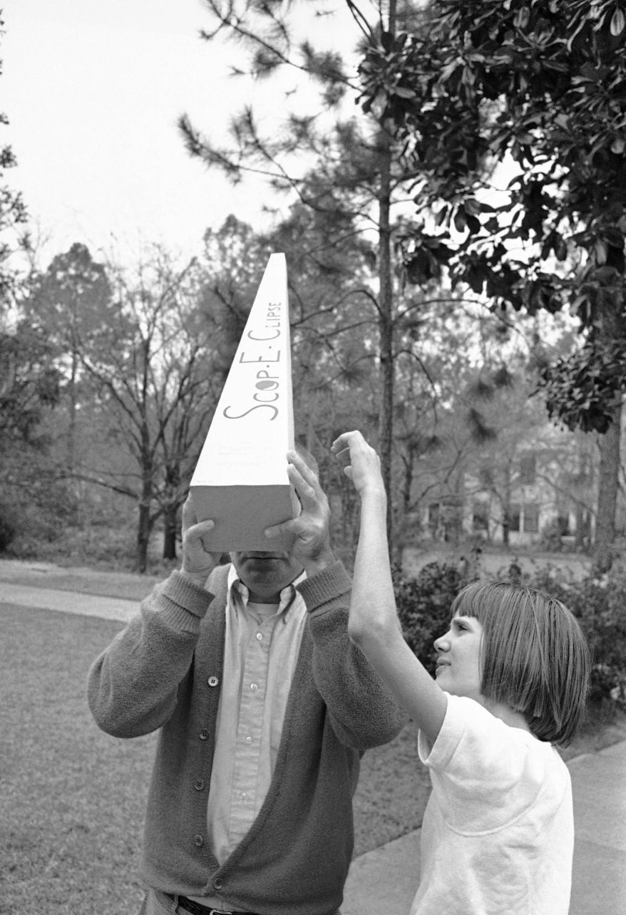 FILE - In this March 7, 1970, file photo, Ginnie Bailey reaches for her eclipse viewer from her father Robert Bailey of Valdosta as the eclipsed sun begins to burn through a cloud cover that has all but obscured a view of the total solar eclipse in Valdosta, Ga. Destinations are hosting festivals, hotels are selling out and travelers are planning trips for the total solar eclipse that will be visible coast to coast on Aug. 21, 2017. A narrow path of the United States 60 to 70 miles wide from Oregon to South Carolina will experience total darkness, also known as totality. (AP Photo/Joe Holloway, Jr., File)