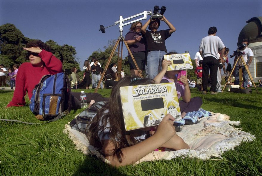FILE - In this June 10, 2002, file photo, Lise Richardson, left, views a partial solar eclipse with her daughters Sophia Richardson, center left, and Samantha, 6, right, at Griffith Observatory in Los Angeles. Destinations are hosting festivals, hotels are selling out and travelers are planning trips for the total solar eclipse that will be visible coast to coast on Aug. 21, 2017. A narrow path of the United States 60 to 70 miles wide from Oregon to South Carolina will experience total darkness, also known as totality. (AP Photo/Krista Niles, File)