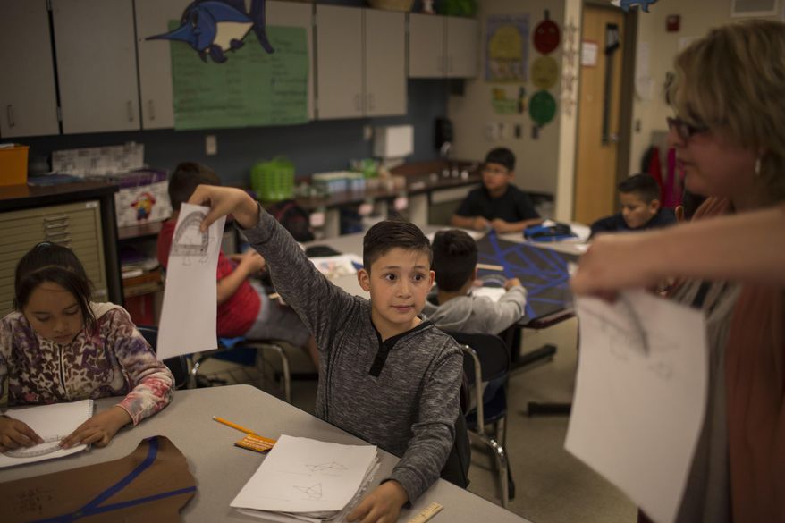 In this Friday, March 31, 2017 photo, a fifth grade student shows his geometry work to a teacher at Columbus Elementary School, in Columbus, New Mexico. American kids living in Mexico make up about 60 percent of Columbus Elementary's student body. Many are the children of parents who were deported and moved here to be able to send their kids to school in the United States. (AP Photo/Rodrigo Abd)