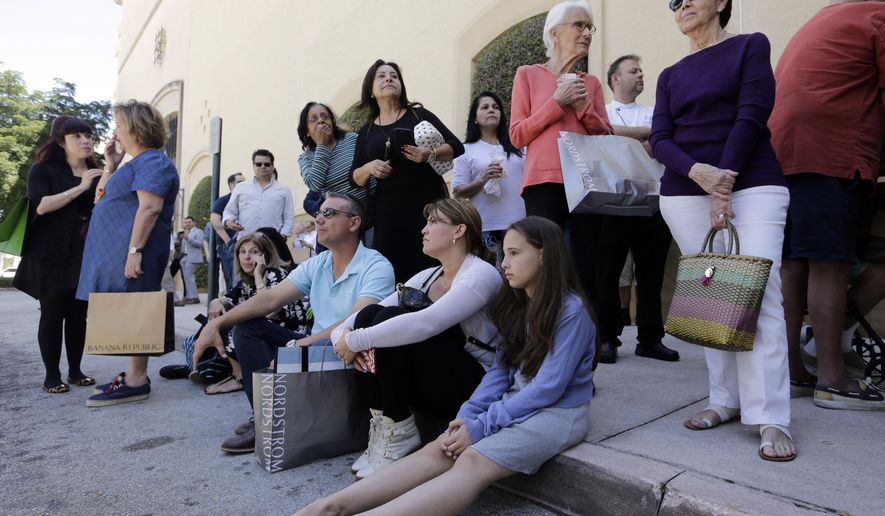 Shoppers Roman Lugo, seated, left, Siuris Rodriguez, center, and Chelsea Lugo, right, sit on the pavement after being evacuated from the Shops at Merrick Park after a shooting, Saturday, April 8, 2017, in Coral Gables, Fla. Alvaro Zabaleta of the Miami-Dade Police Department says detectives have responded to the scene of the shooting in the upscale shopping mall in South Florida. (AP Photo/Lynne Sladky)
