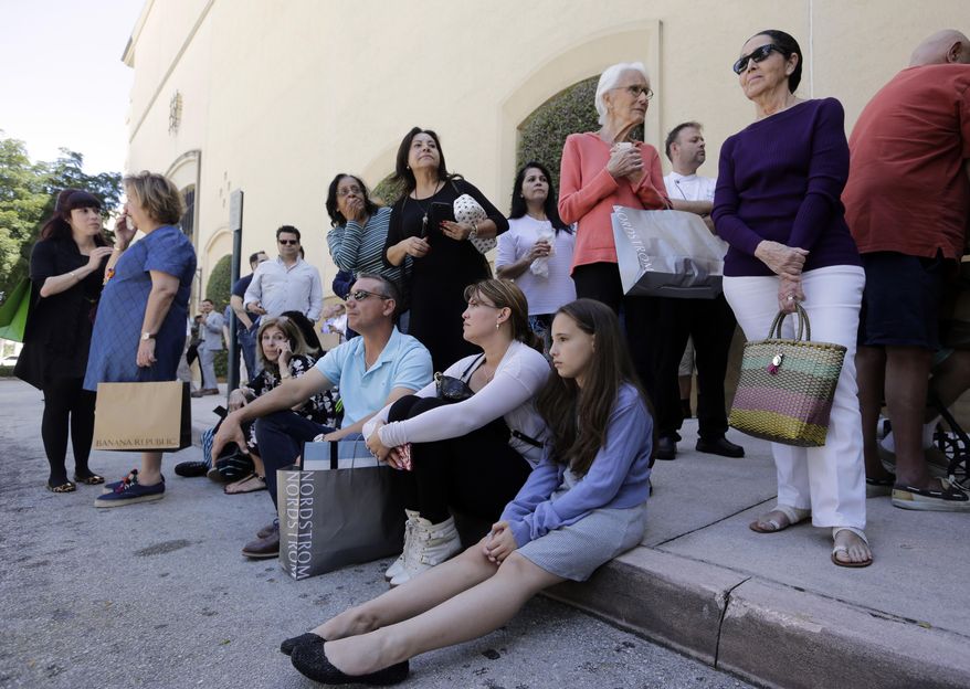Shoppers Roman Lugo, seated, left, Siuris Rodriguez, center, and Chelsea Lugo, right, sit on the pavement after being evacuated from the Shops at Merrick Park after a shooting, Saturday, April 8, 2017, in Coral Gables, Fla. Alvaro Zabaleta of the Miami-Dade Police Department says detectives have responded to the scene of the shooting in the upscale shopping mall in South Florida. (AP Photo/Lynne Sladky)