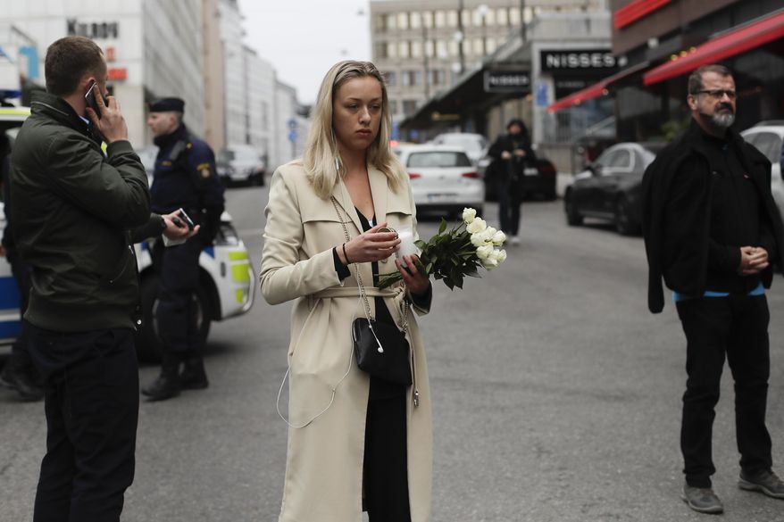 A woman prepares to offer flowers near the department store Ahlens following a suspected terror attack in central Stockholm, Sweden, Saturday, April 8, 2017. A Swedish prosecutor says a person has been formally identified as a suspect "of terrorist offenses by murder" by driving a hijacked truck into a crowd of pedestrians. (AP Photo/Markus Schreiber)
